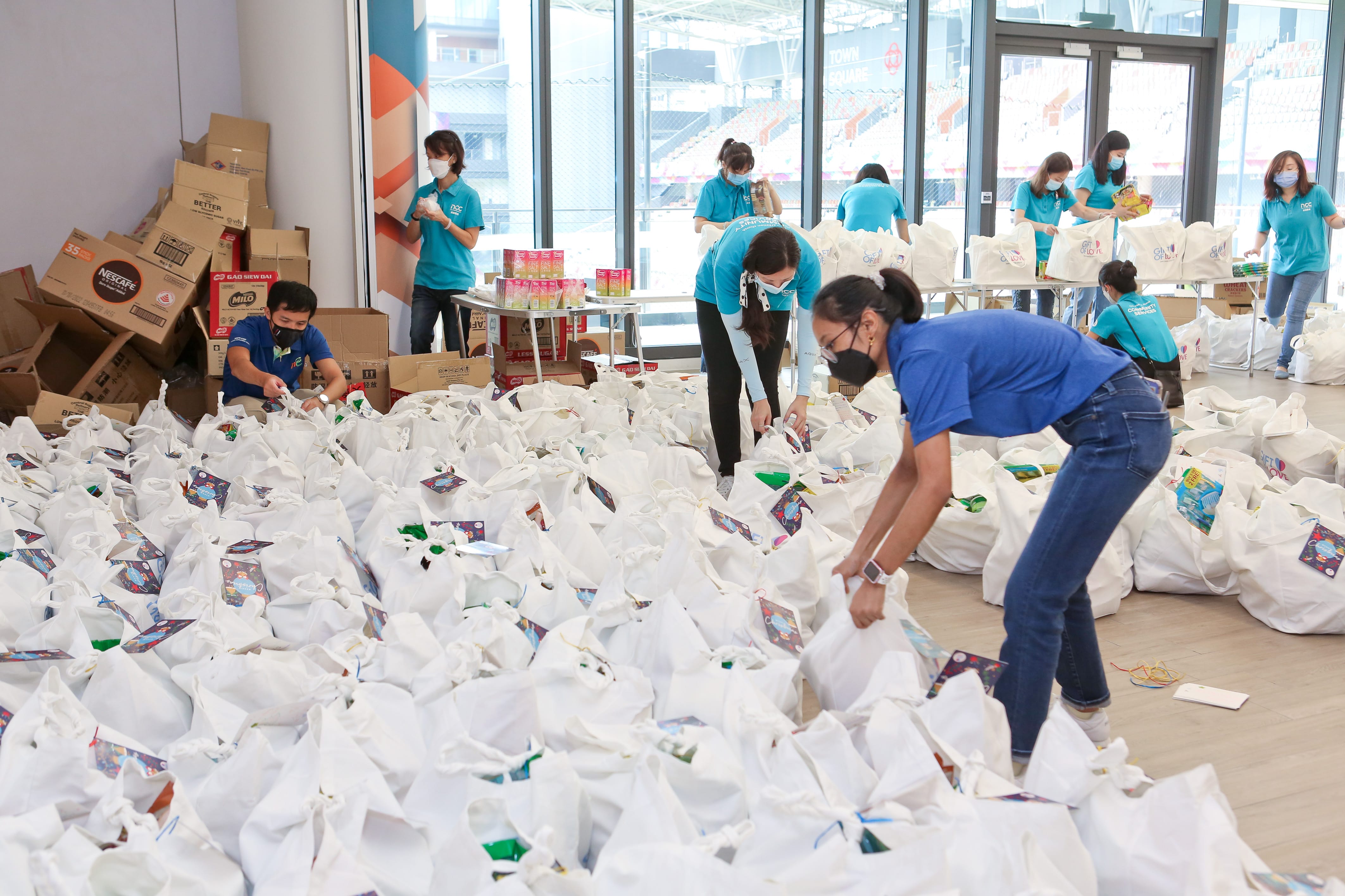 People in blue shirt preparing and organizing numerous white tote bags indoors, surrounded by cardboard boxes.